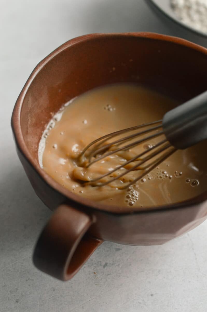 Whisking milk, maple syrup, peanut butter and vanilla in a mug.