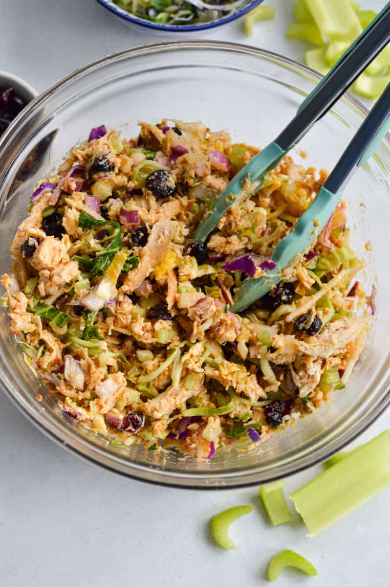 Mixing shredded cooked chicken, red onion, celery, dried cranberries and kale slaw with honey mustard vinaigrette to make a no mayo chicken salad.