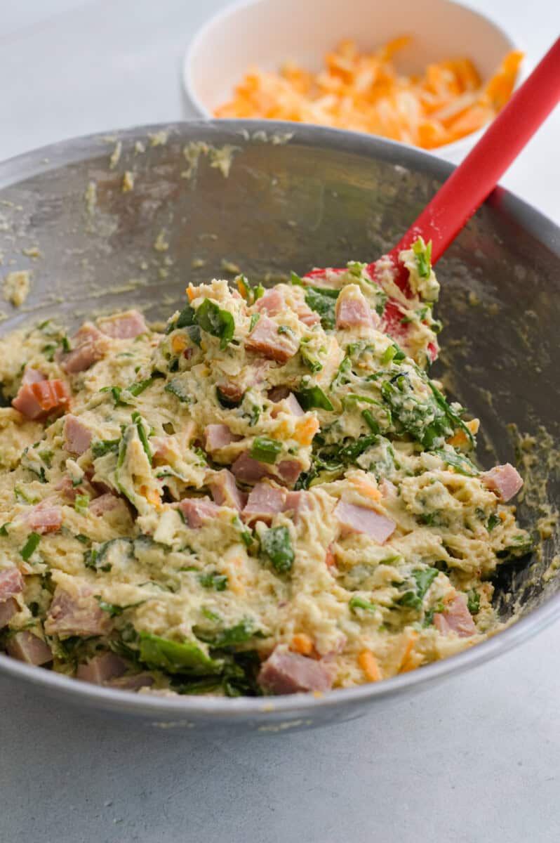 Mixing spinach, chives, shredded cheese and ham into biscuit dough.