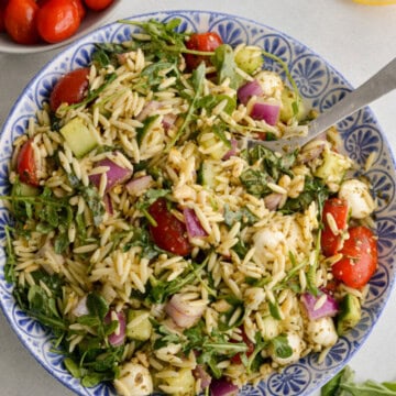 Birds eye of bowl of orzo pesto salad with arugula, cherry tomatoes, red onion, cucumber and bocconcini.