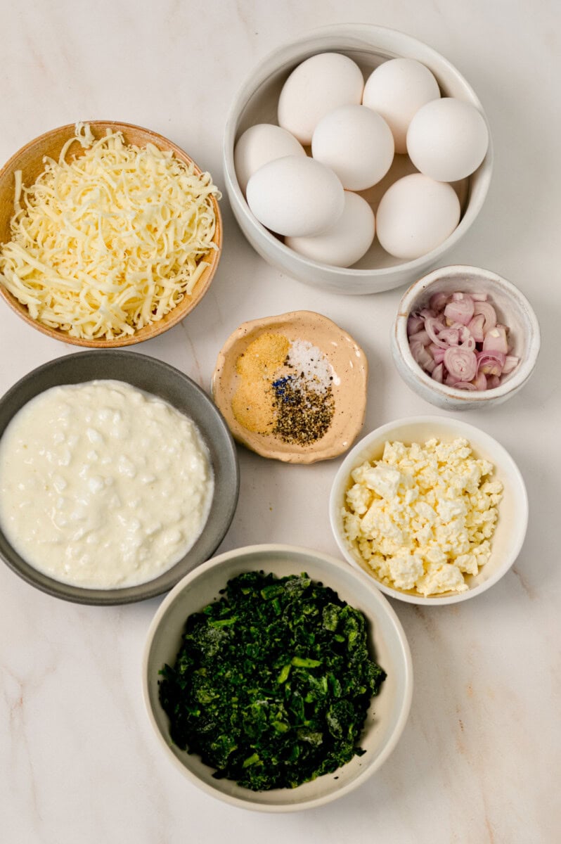 Ingredients for casserole including eggs, cheese, spinach, mozzarella, shallots, cottage cheese and spices