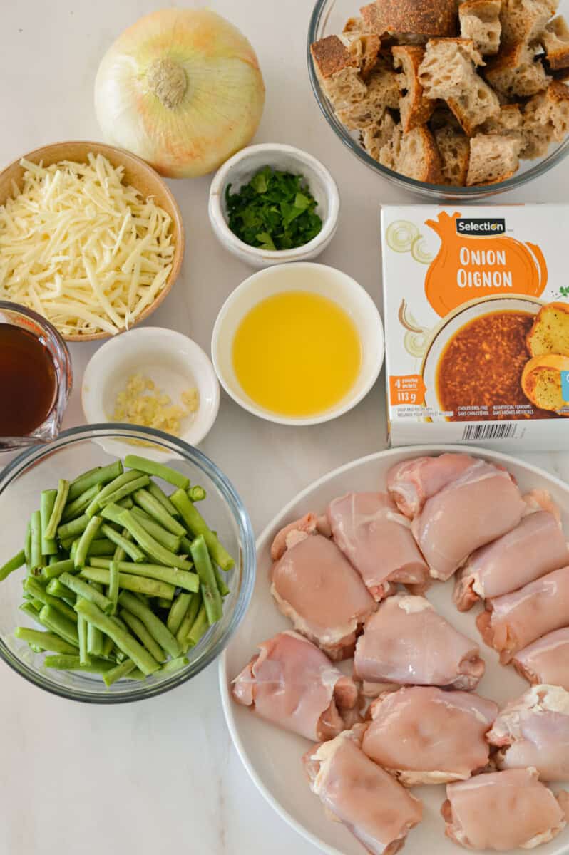 Ingredients for French Onion Chicken including chicken thighs, onion, onion soup mix, cheddar, beans, butter, parsley and garlic