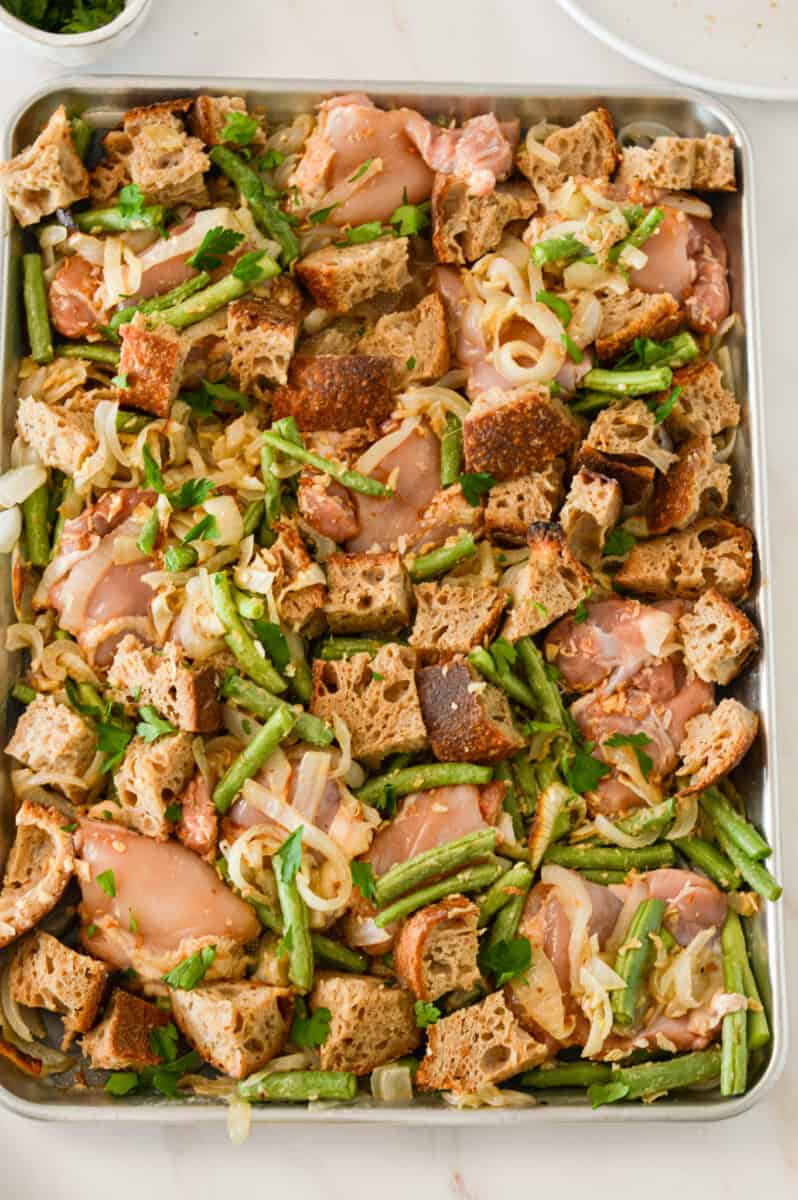 Chicken thighs added to the sheet pan with green beans and cut sourdough bread