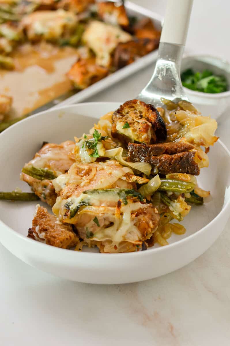 French onion chicken being added to a bowl from the sheet pan