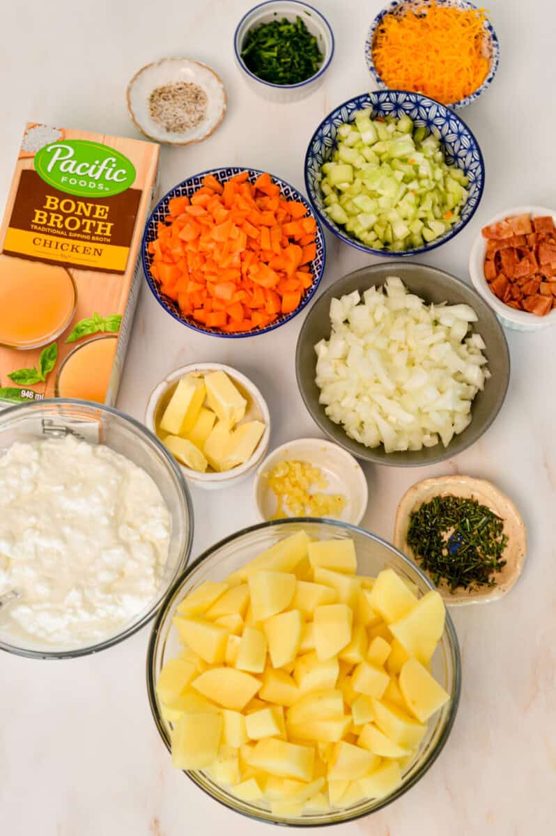 Ingredients for soup including potatoes, cottage cheese, carrots, celery, onion, chicken bone broth, herbs, spices, garlic, turkey bacon and cheese