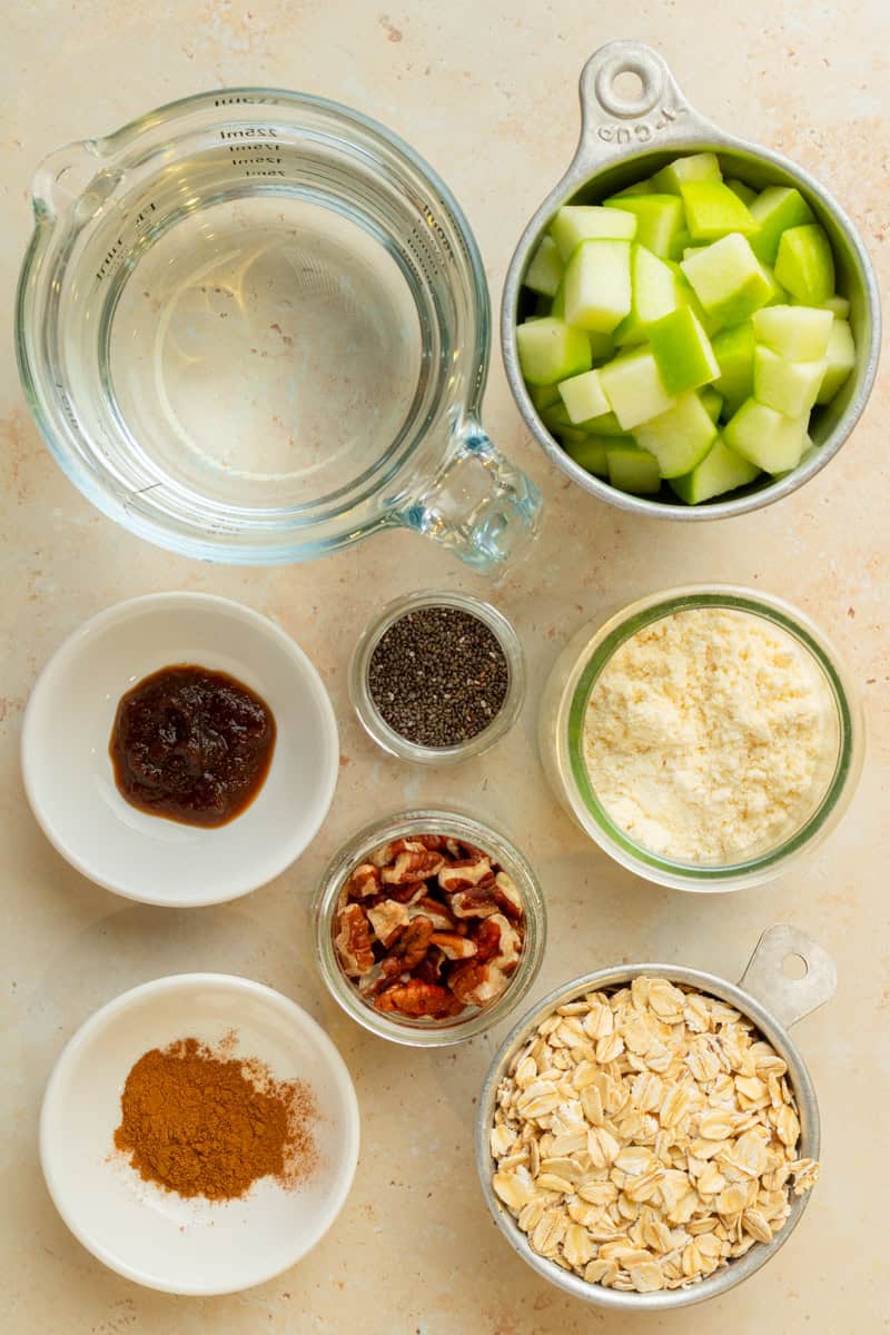 Ingredients for oatmeal including apples, apple butter, cinnamon, oats, pecans, vanilla protein, and chia seeds