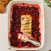 Birdseye view of knife slicing baked feta cheese dip with cranberries