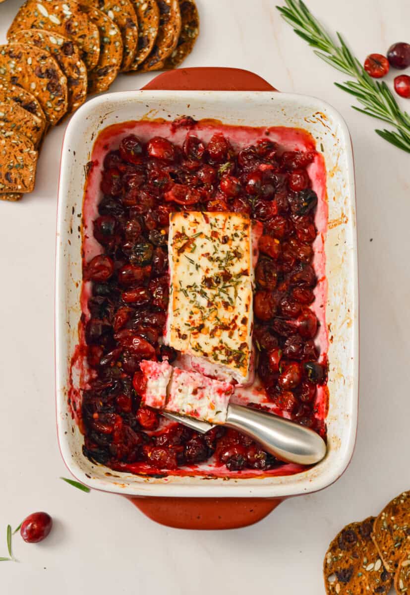Birdseye view of knife slicing baked feta cheese dip with cranberries