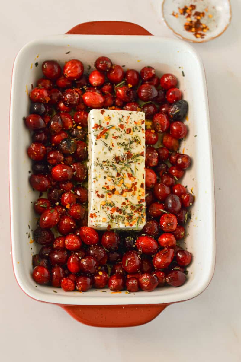 Feta cheese block added to the baking dish with more rosemary, chili flakes and black pepper on top