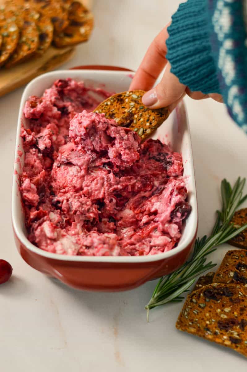 Scooping the combined creamy version of baked feta dip with a cracker