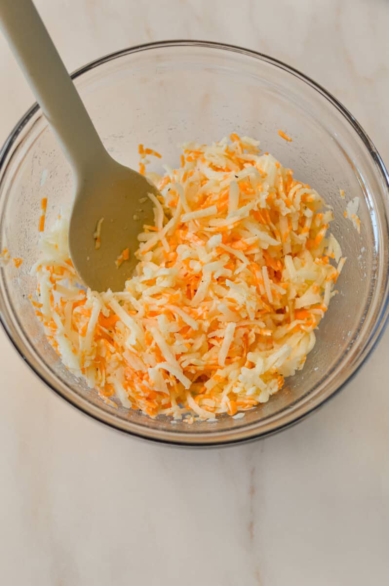 Overhead shot of cheese, spices and hashbrowns in a mixing bowl