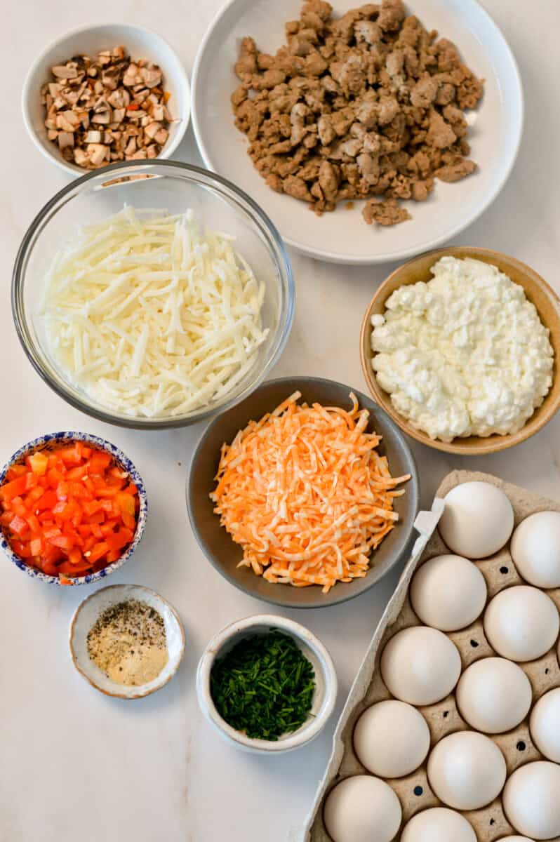 Ingredients for the hashbrown egg cups including sausage, vegetables, shredded cheese, shredded hashbrowns, eggs, cottage cheese, chives and spices