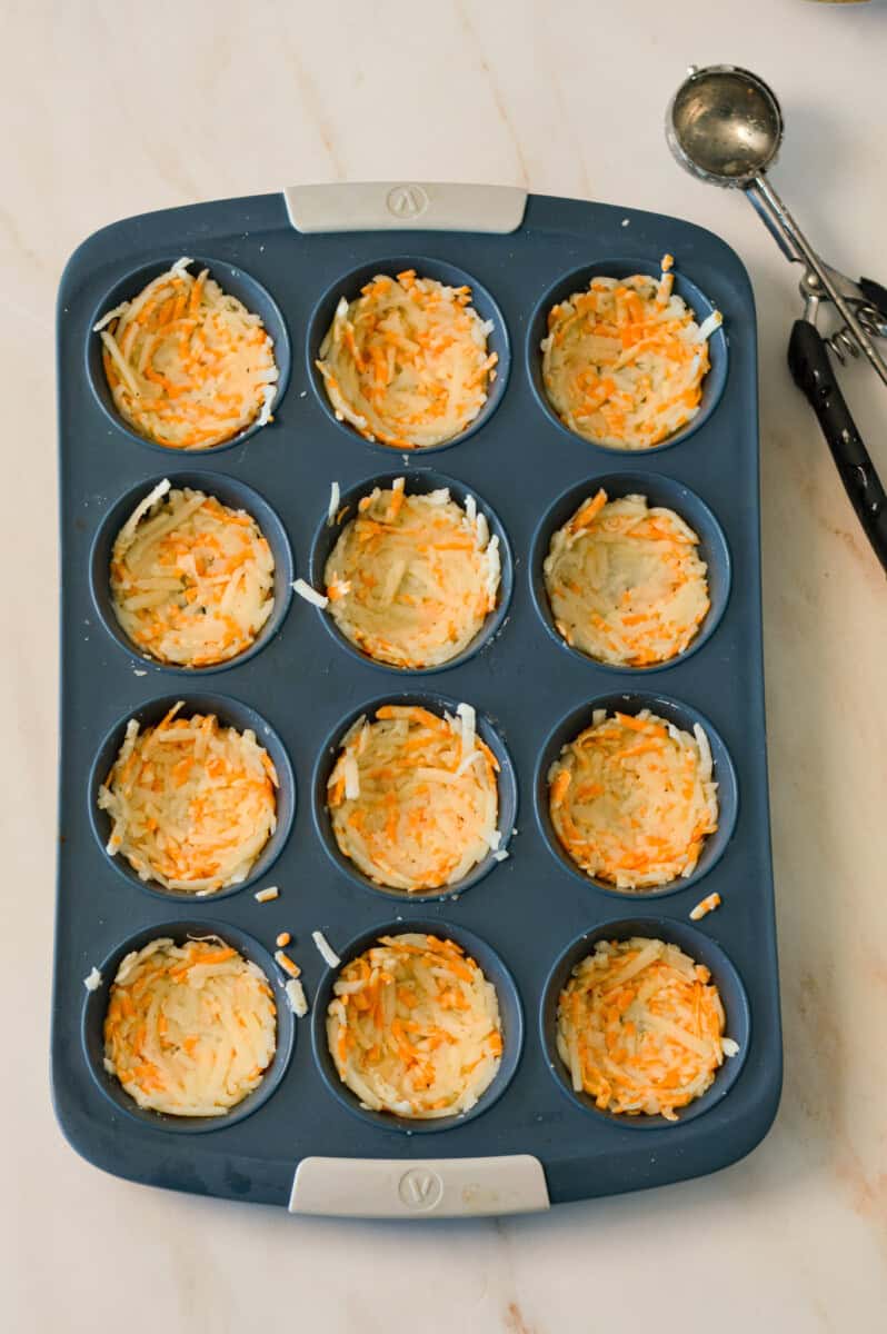 Hashbrowns mixture pressed into nests in a muffin tray