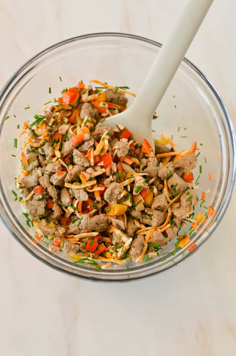 Sausage, vegetables and cheese being combined in a mixing bowl