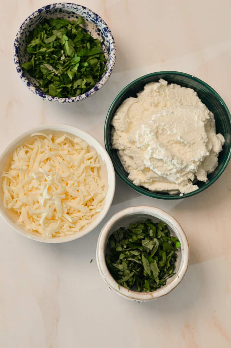 Ingredients for ricotta topping including ricotta cheese, cottage cheese, mozzarella cheese, fresh parsley, and fresh basil