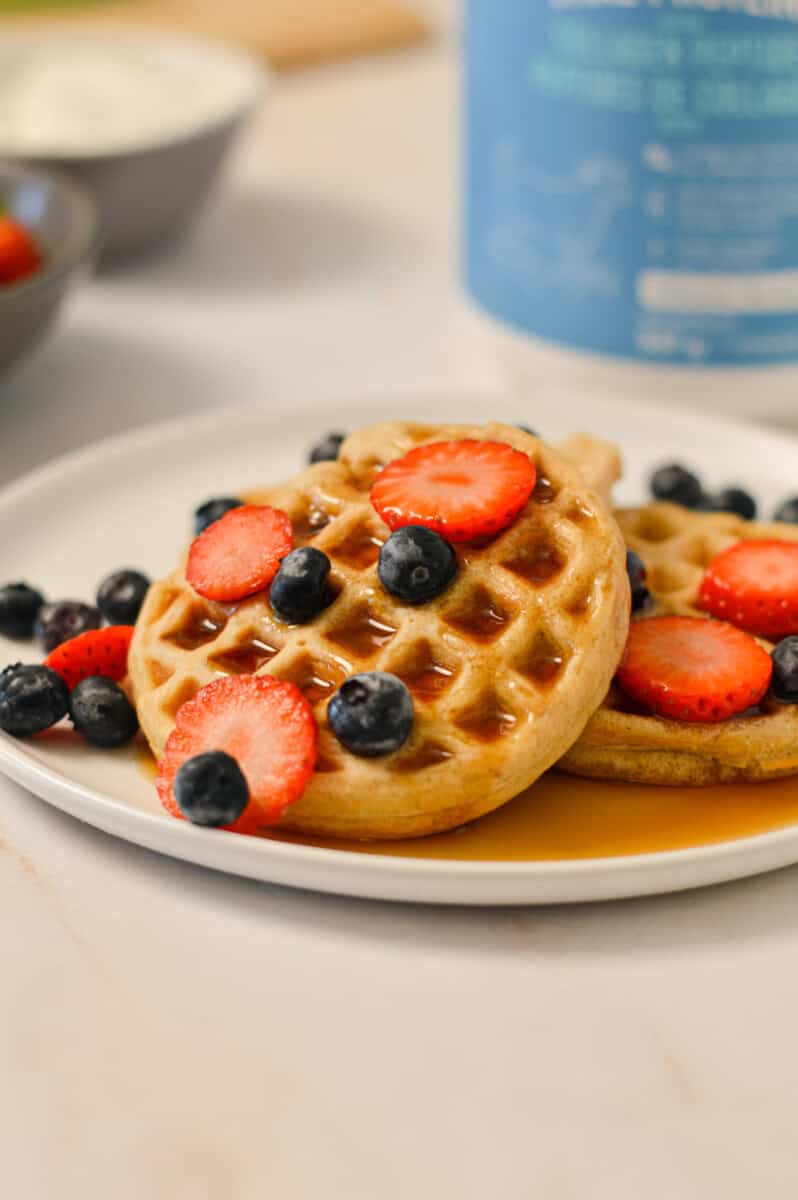 Close up of waffles on a plate with strawberries, blueberries and maple syrup