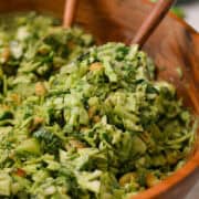 Salad tong lifting up green goddess salad out of a large salad bowl