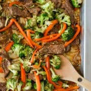 Birdseye of sheet pan beef and broccoli with spatula lifting some pieces up