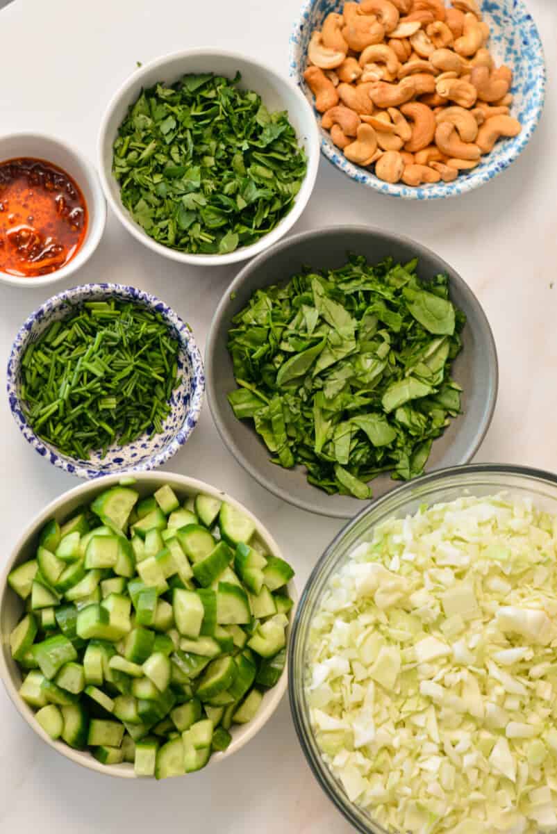 Ingredients for Green Goddess Salad including spinach, cucumber, green cabbage, cashews, chili oil and fresh herbs.