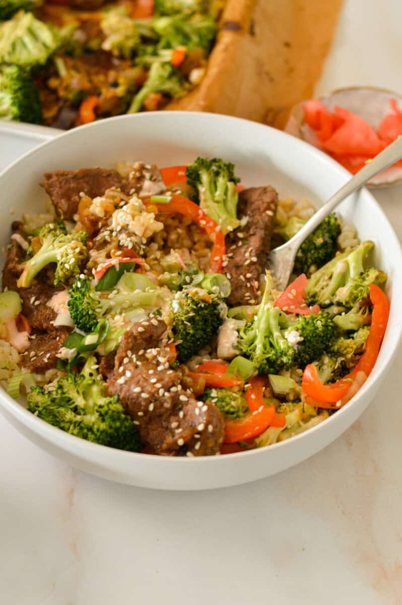 Sheet pan in a bowl with rice and sriracha mayo with a fork in the bowl