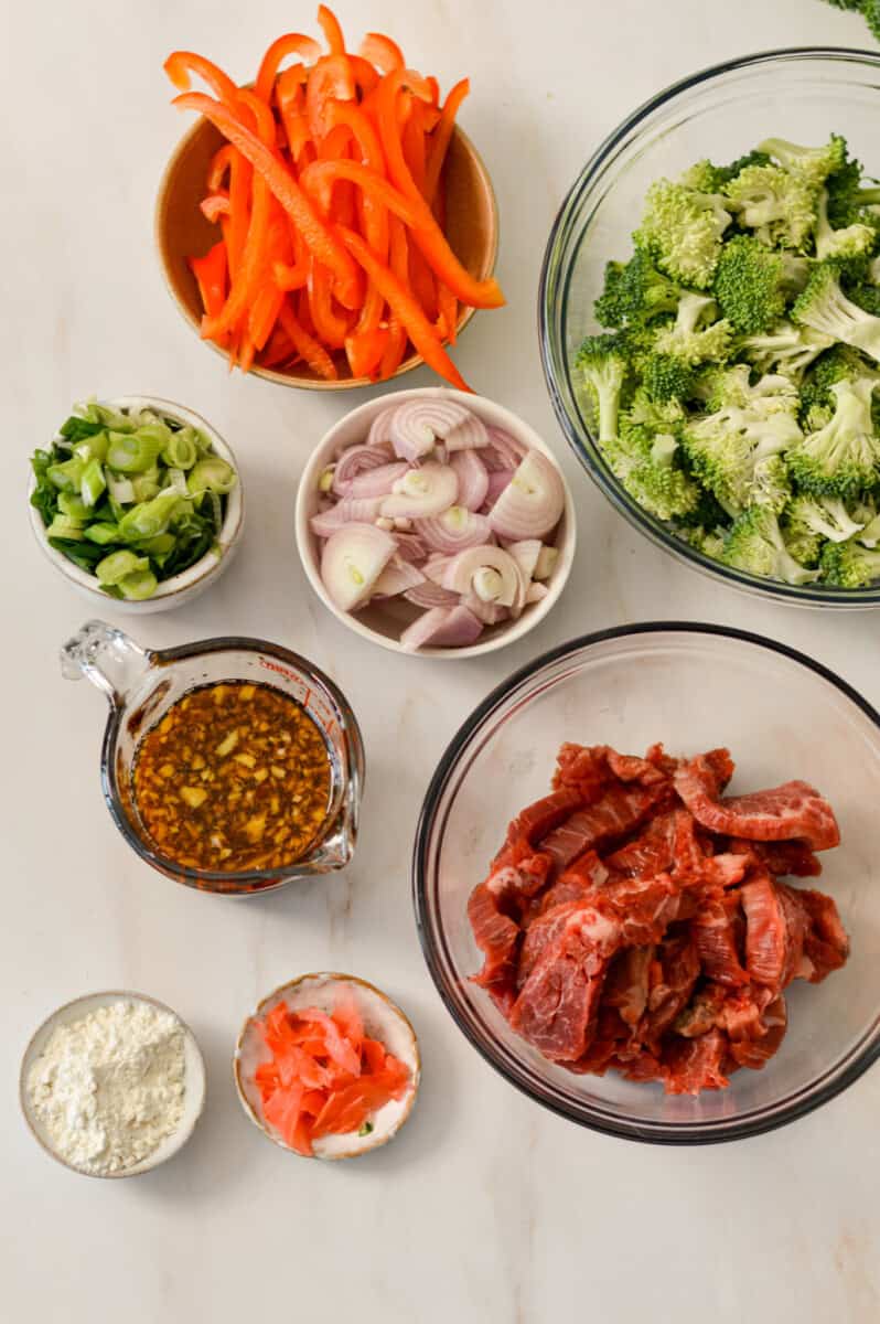 Ingredients for sheet pan dinner including flank steak, broccoli, red bell pepper, shallot, sauce, flour, and red pepper flakes.