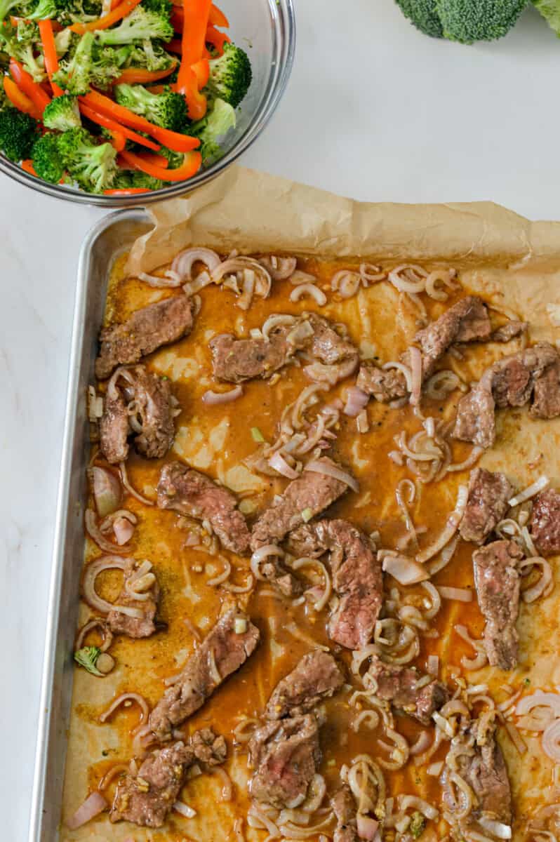 Broccoli and bell pepper removed from the sheet pan in a bowl with just the steak and onion left on the sheet pan