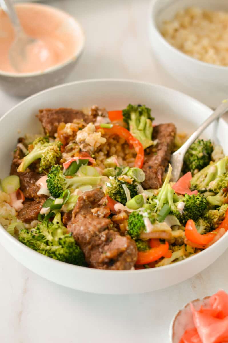 Close up of steak sheet pan dinner served over rice in a bowl with a fork