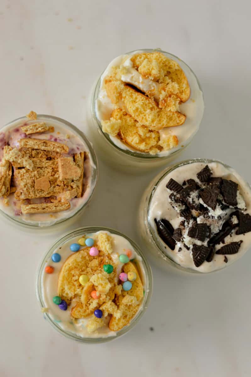 Birdseye shot of four high-protein cheesecake jars with different flavour variations including oreo, banana cream pie, classic cheesecake and birthday cake