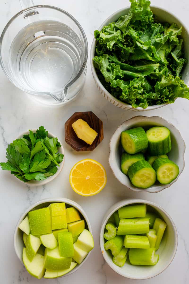 Ingredients for blender green juice including kale, cucumber, water, lemon, ginger, celery, apple and parsley