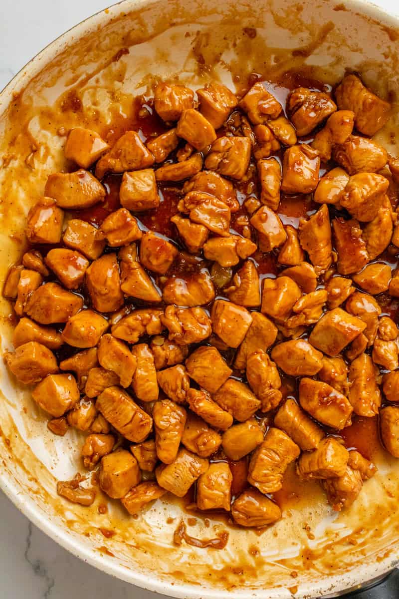 Chicken being cooked in a pan with teriyaki sauce added