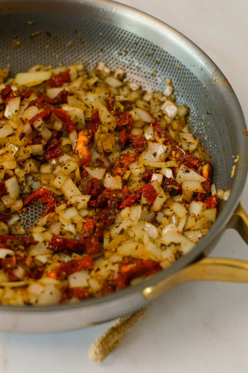 Onion, spices and sun dried tomatoes in a pan