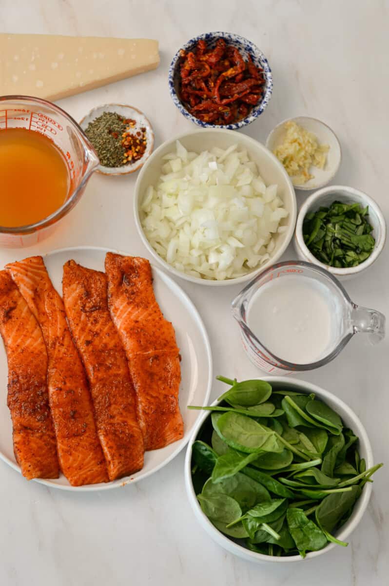 Ingredients for marry me salmon including salmon, spinach, onion, sun dried tomatoes, spinach, coconut milk, vegetable broth, fresh basil, garlic, spices, and parmesan