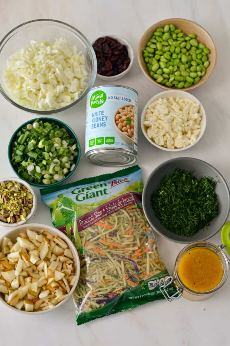 Ingredients for pear and fennel salad including pears, navy beans, edamame, green onions, coleslaw mix, fennel, fresh dill, red onion, and lemon dijon dressing