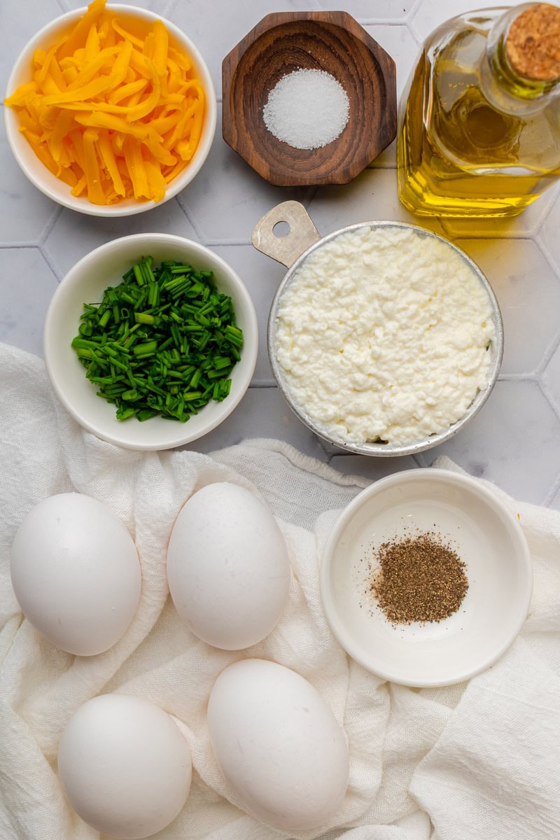 Ingredients for cottage cheese eggs including eggs, cottage cheese, shredded cheddar cheese, chives, olive oil, salt and pepper.