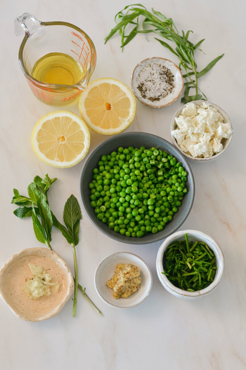 Ingredients for green pea hummus including sweet green peas, lemon, feta, garlic, olive oil, salt and pepper, fresh mint, fresh tarragon, fresh chives, and dijon.