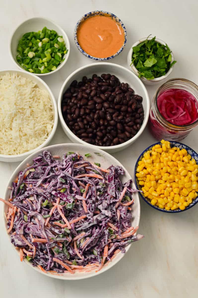 Ingredients to build the pulled pork bowls including coleslaw, corn, green onions, sriracha mayo, pickled onions, rice and cilantro