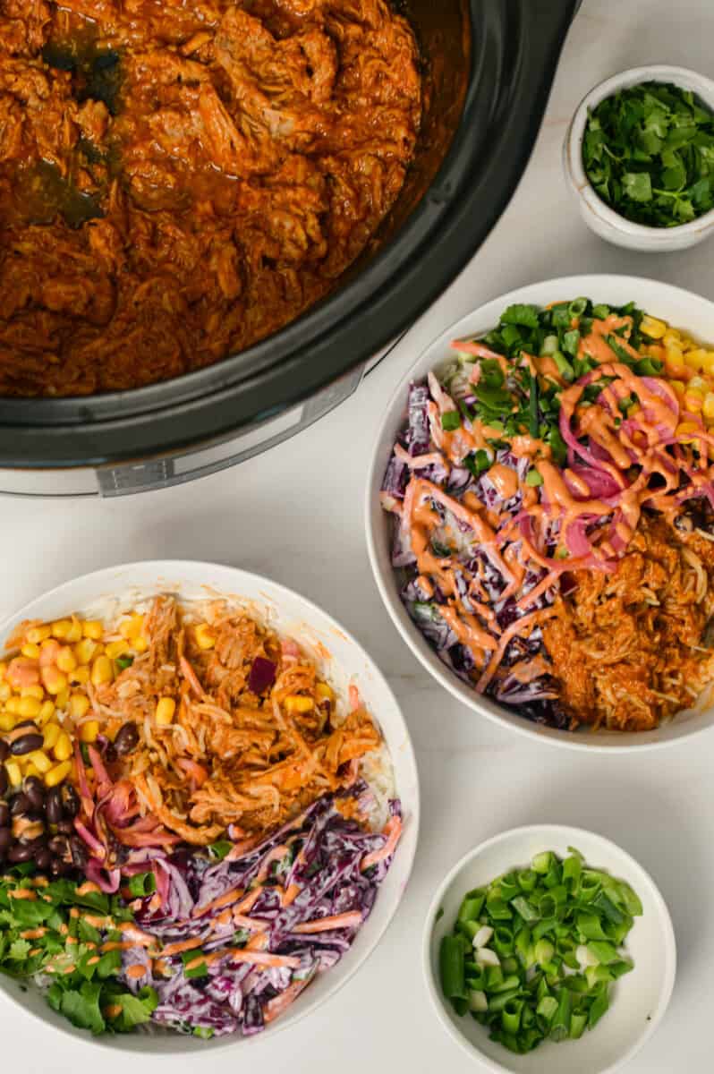 Birdseye of two pulled pork bowls with a crockpot next to them.