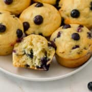 Close up of Blueberry Greek Yogurt Muffins on a plate. One has a bite taken out of it.