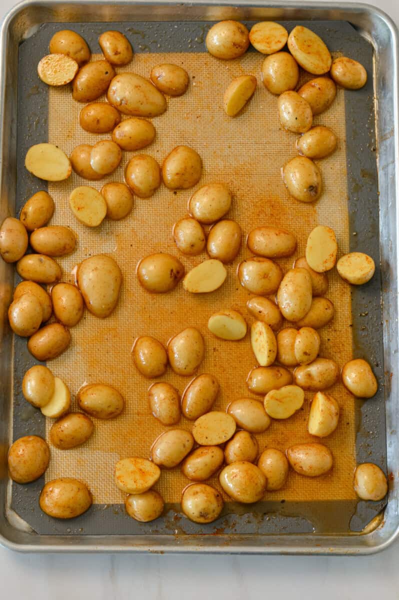 Sliced baby potatoes on a baking sheet with spices.