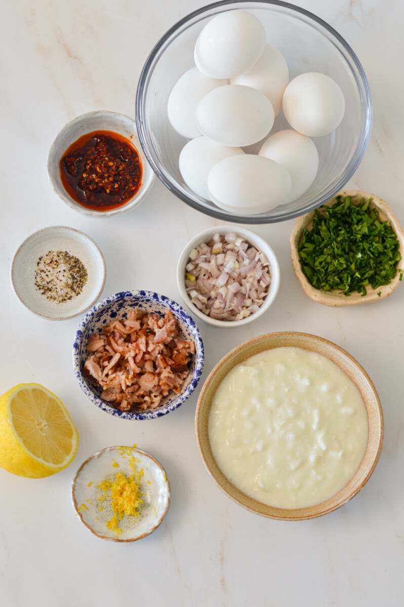 Ingredients for spicy egg salad including eggs, cottage cheese, bacon, lemon, shallots, chili crunch, spices, and cilantro.