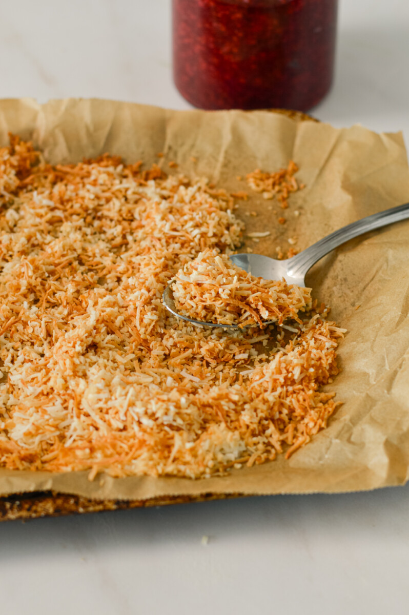 Spoon lifting up toasted coconut on parchment paper.