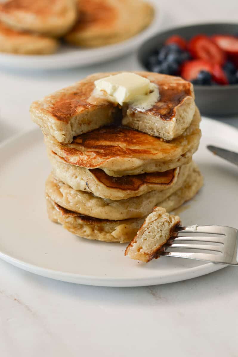 Stack of banana cottage cheese pancakes on a plate with butter. A fork has taken a bite out of it.