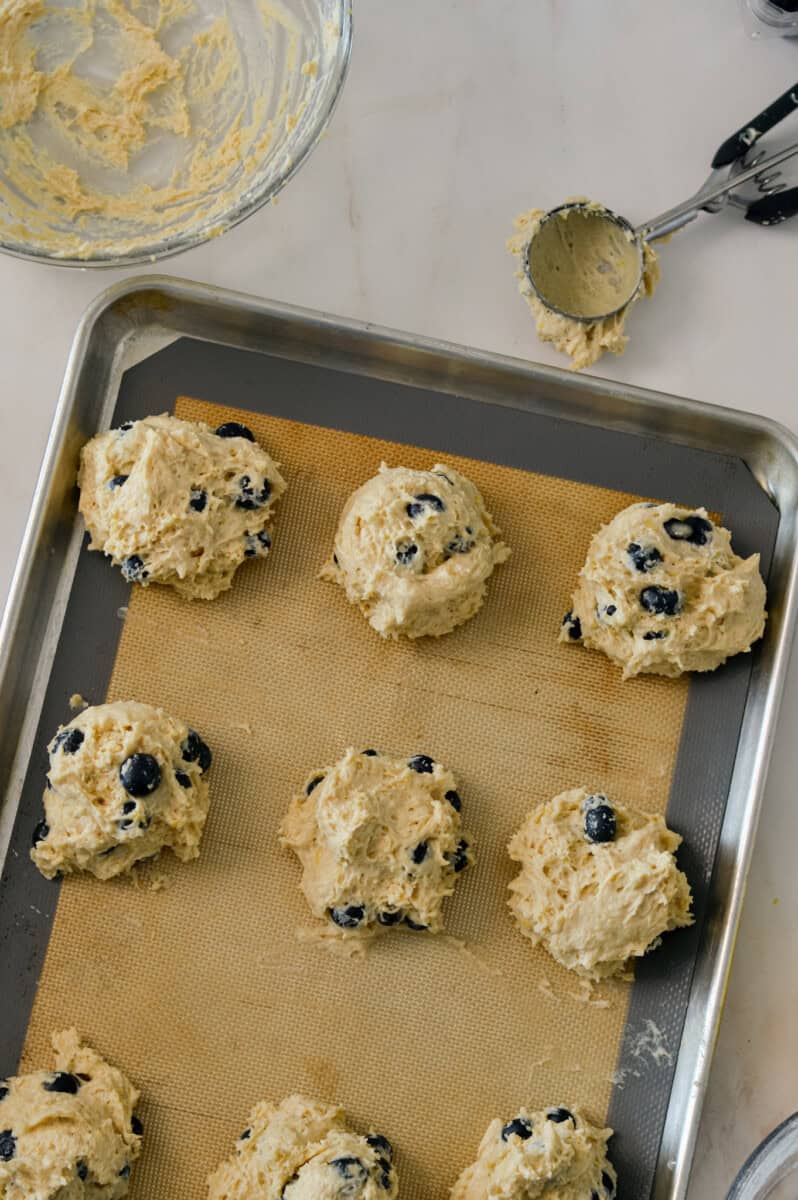 Raw biscuits being scooped and portioned onto a baking sheet.