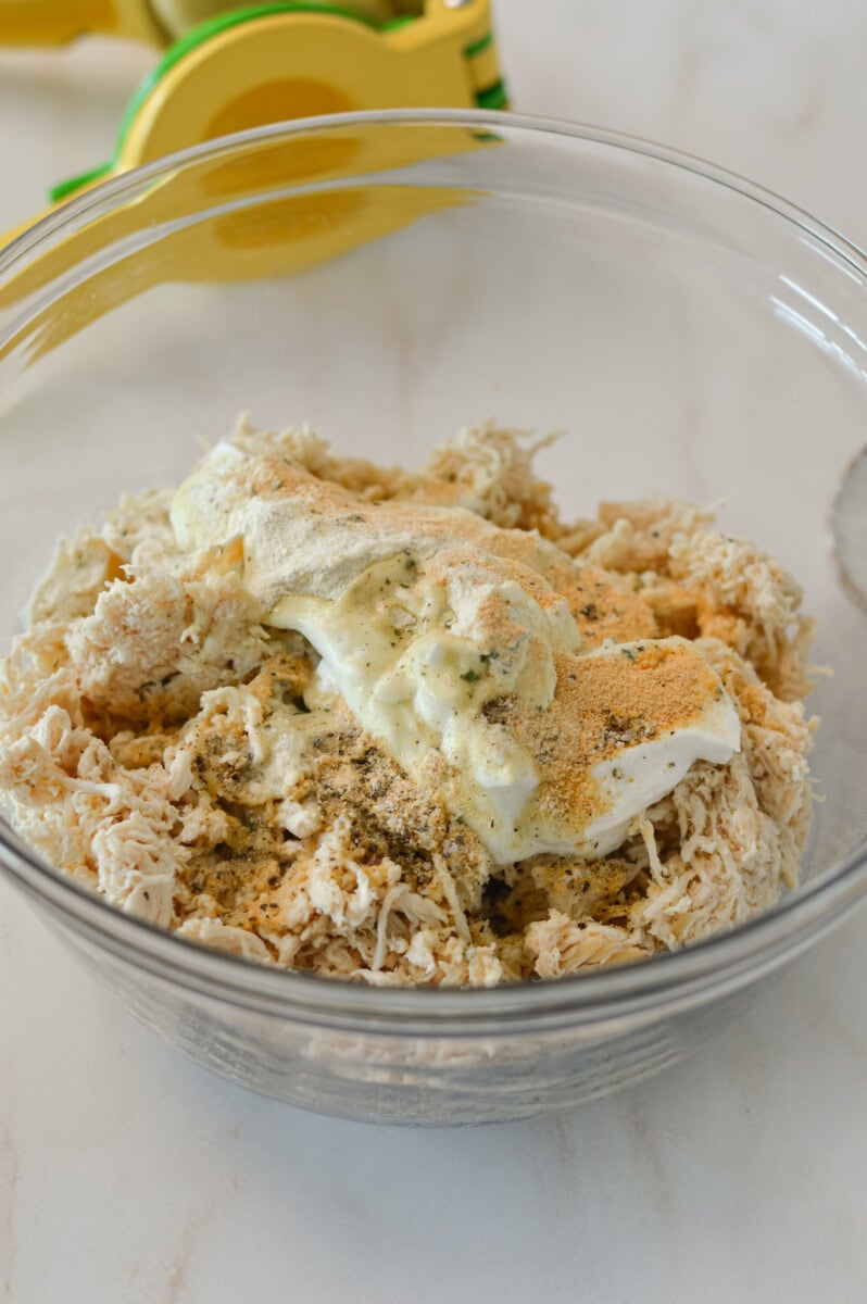 Shredded chicken in a bowl with Greek yogurt, mayo and spices.