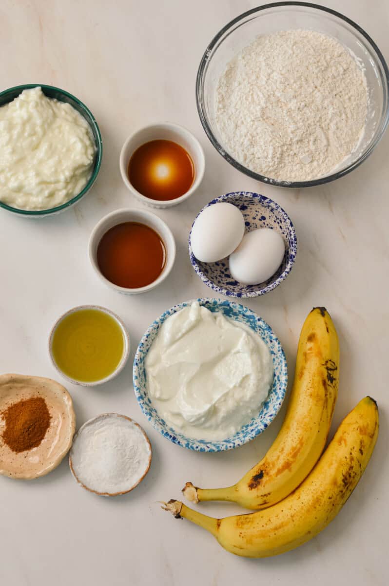 Ingredients for pancakes including cottage cheese, Greek yogurt, bananas, vanilla, eggs, flour, maple syrup, olive oil, cinnamon, baking powder and salt.