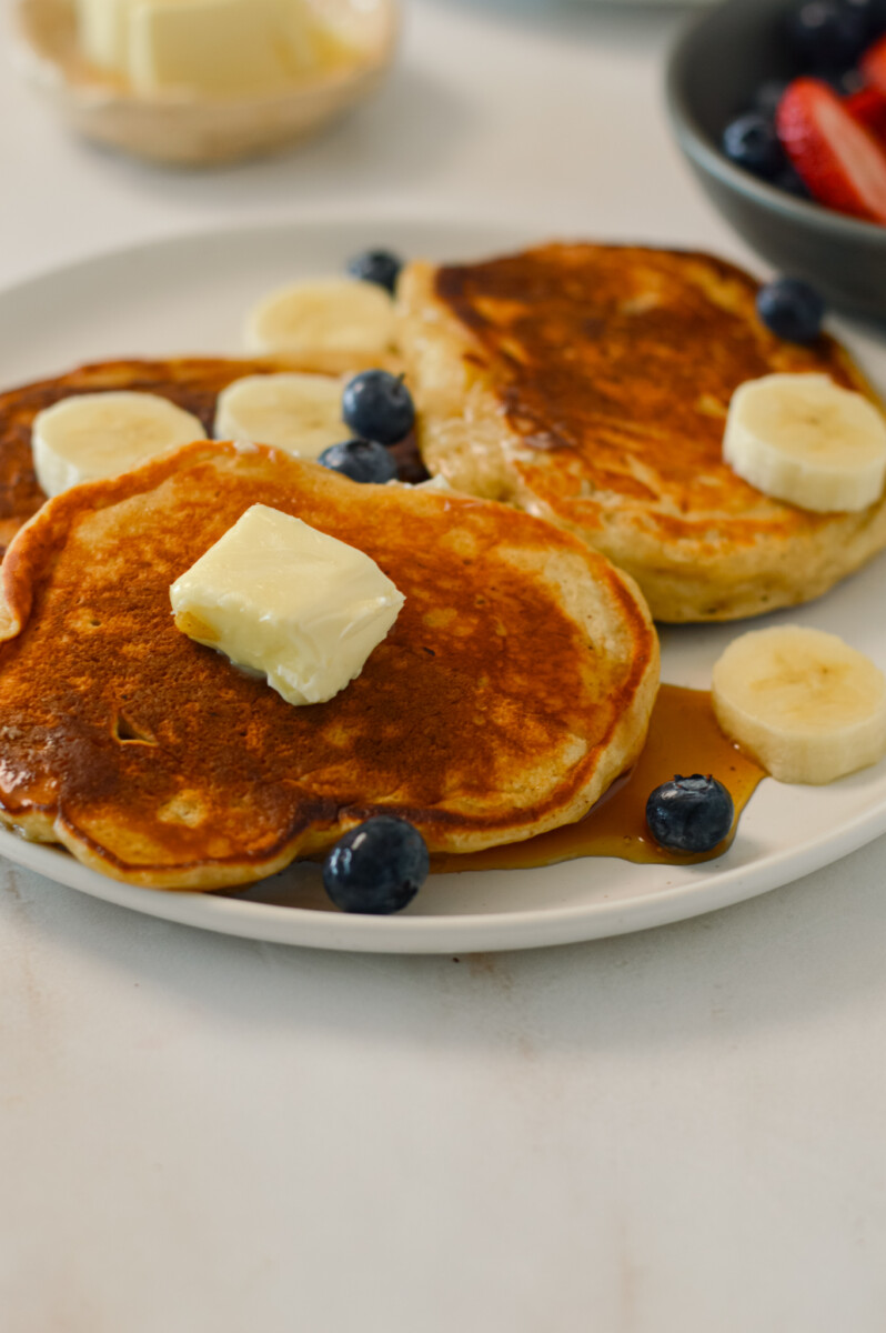 Cottage cheese pancakes on a plate topped with butter, berries and maple syrup.