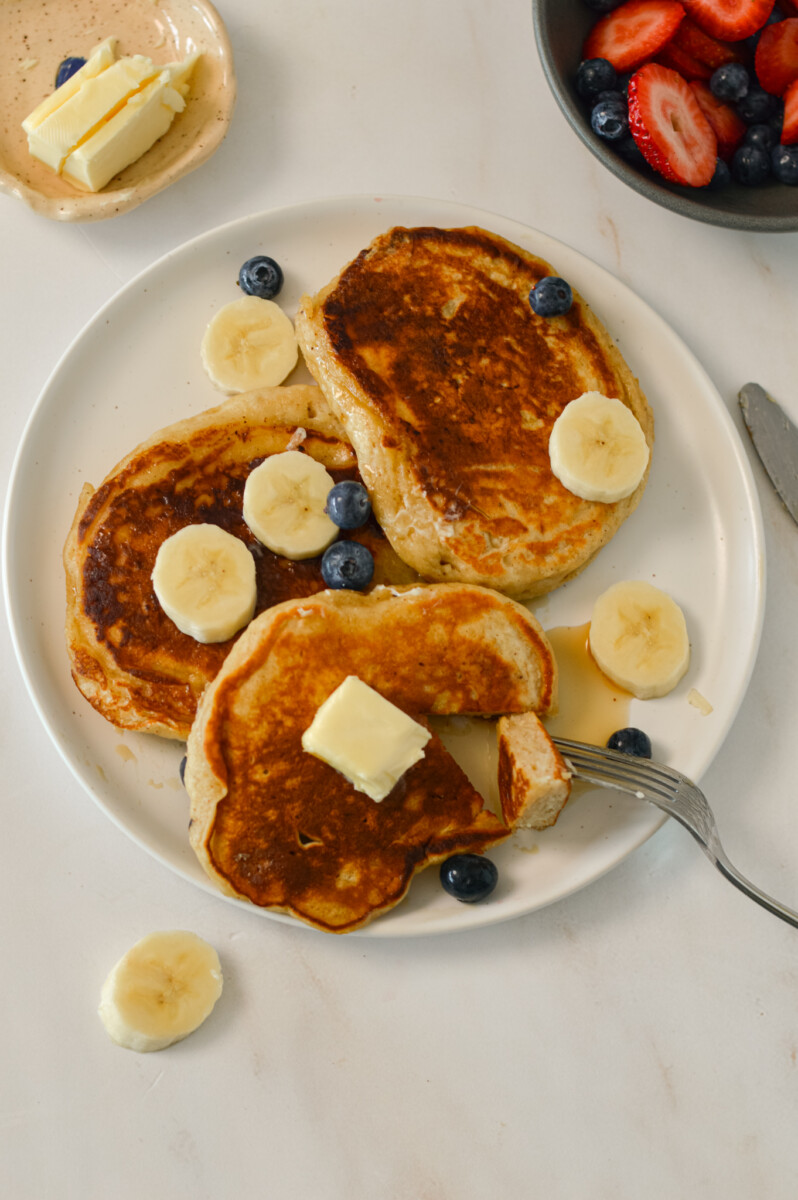 Birdseye of pancakes with bananas, blueberries, strawberries, maple syrup and butter.