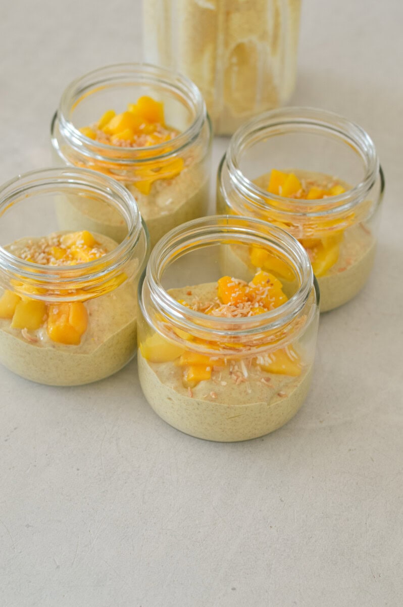 Mango pudding divided into jars, topped with frozen mango and shredded coconut.