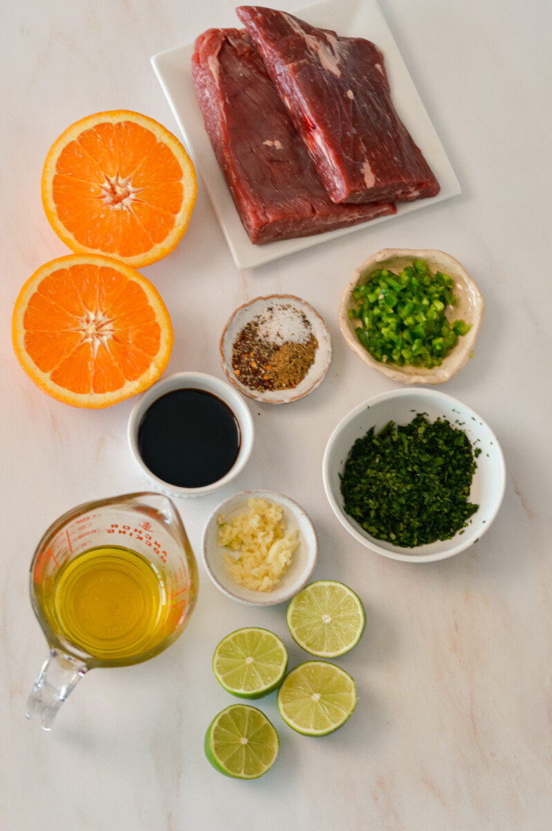 Ingredients for the steak tacos including flank steak, orange, soy sauce, olive oil, cilantro, lime, garlic, jalapeño and spices.