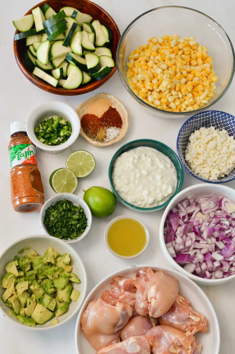 Ingredients for street corn chicken rice bowls including chicken thighs, frozen corn, cotija cheese, red onion, zucchini, lime, cilantro, tajin, jalapeño, cottage cheese, avocado and spices.